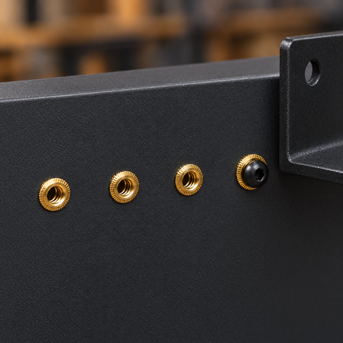 Finished result: several brass M3 rivet nut flanges sitting flush in a steel panel, one with an M3 bolt holding a small bracket
